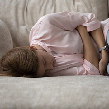 Sarah lying on a couch holding her stomach, crippled with worry