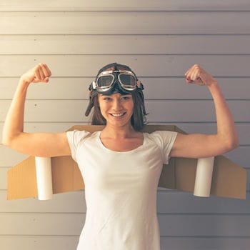 A young woman wearing an old pilot's cap and cardboard wings, flexing her arm muscles