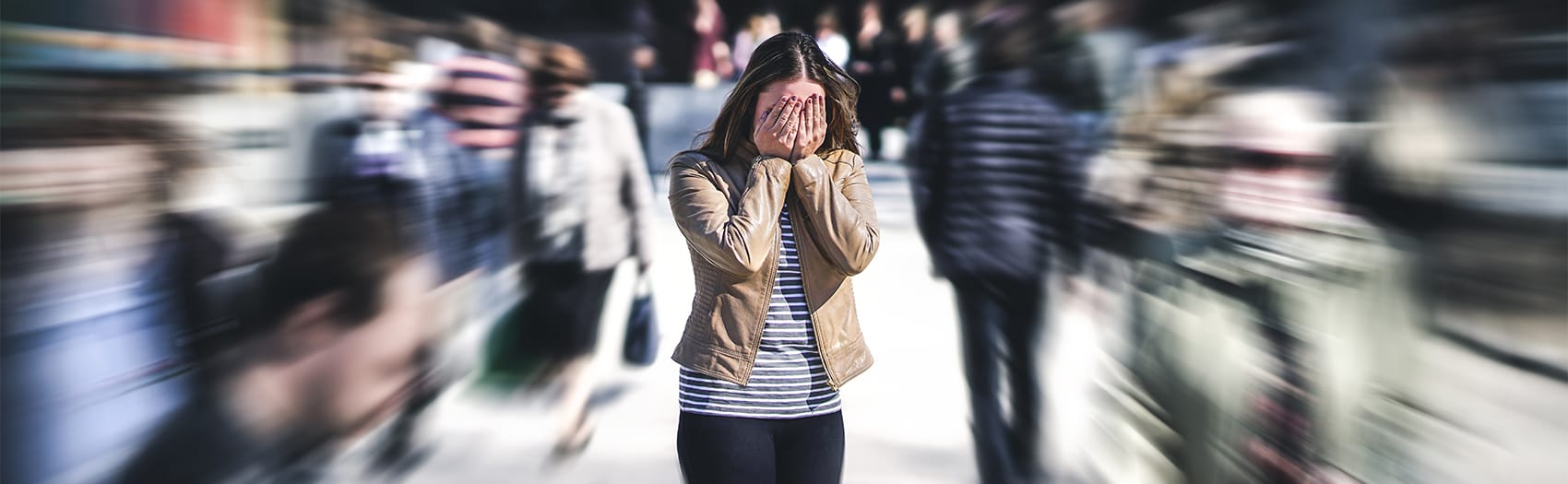 A woman feeling overwhelmed in a crowd, holding her face with her hands