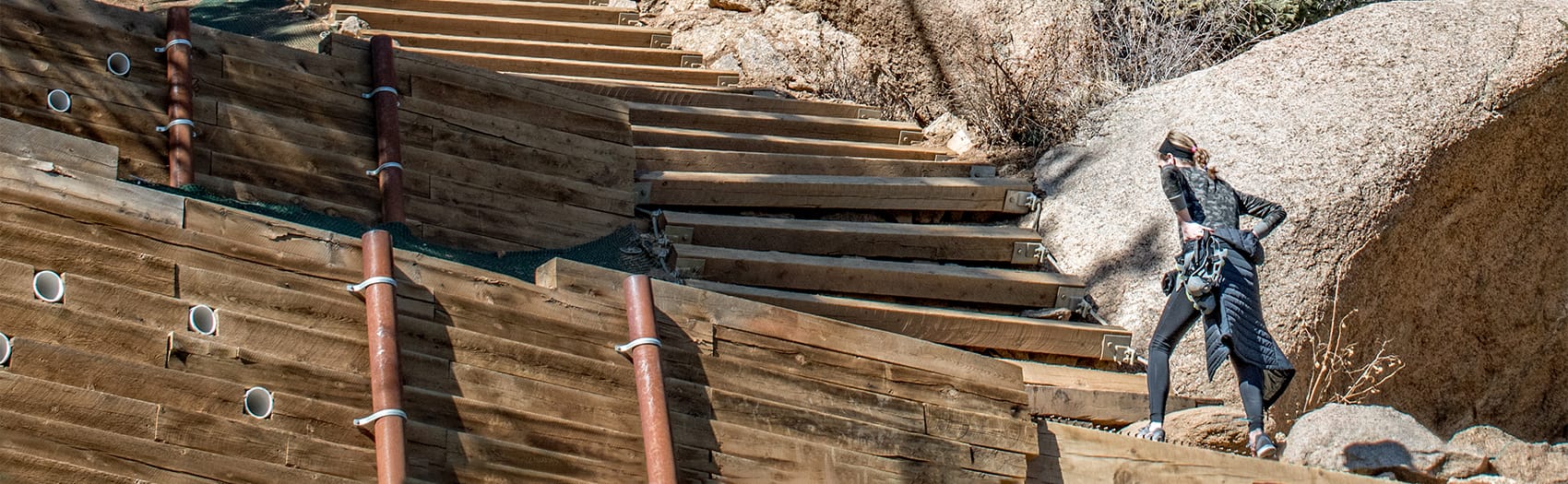 An adventurous woman climbing a wooden staircase up a mountainside