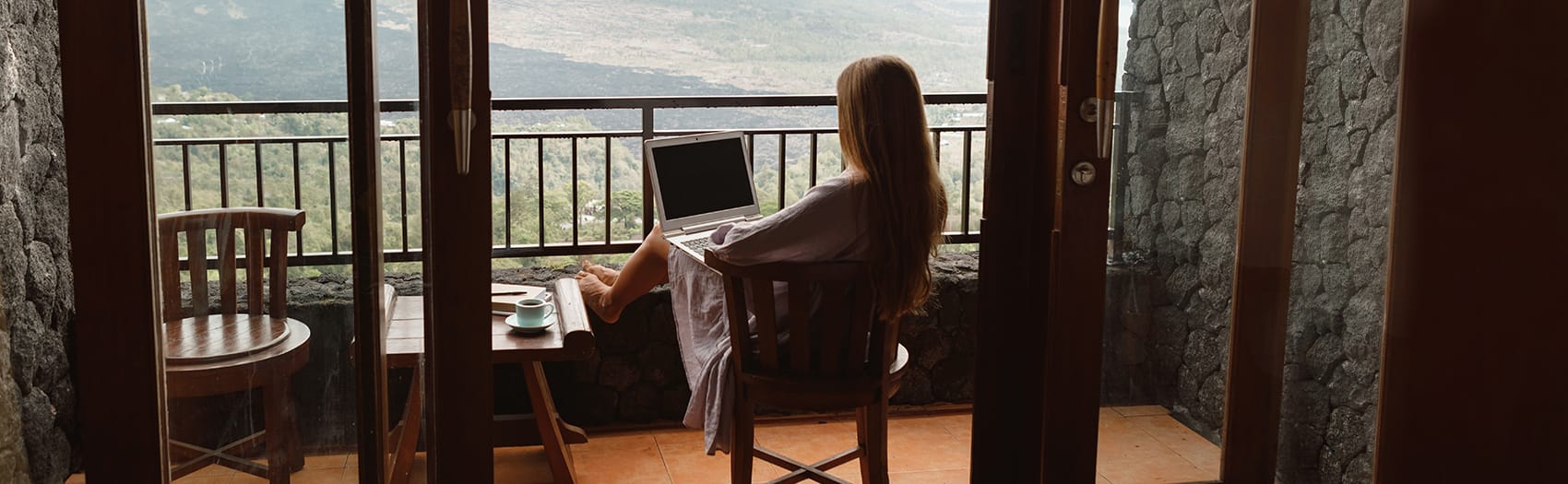 A woman sitting on a porch with her laptop, overlooking a vast forest valley