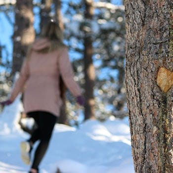 A girl running in the snow past a tree with a heart carved in it