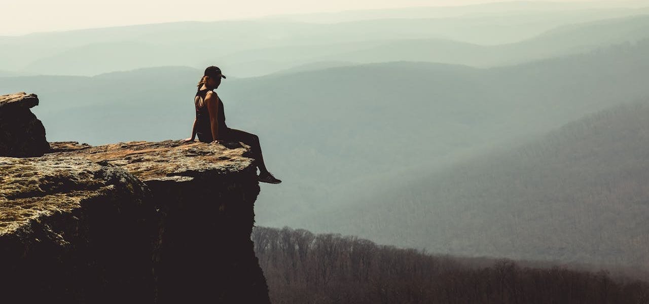 A woman boldly sitting on a ledge above rolling forest hills