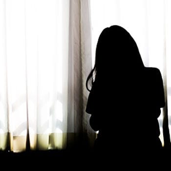 A silhouette of Jennifer sitting in the dark with the shades closed
