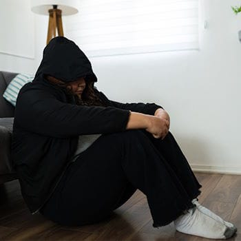 Jessie in a hoodie, sitting on the floor and leaning against a couch